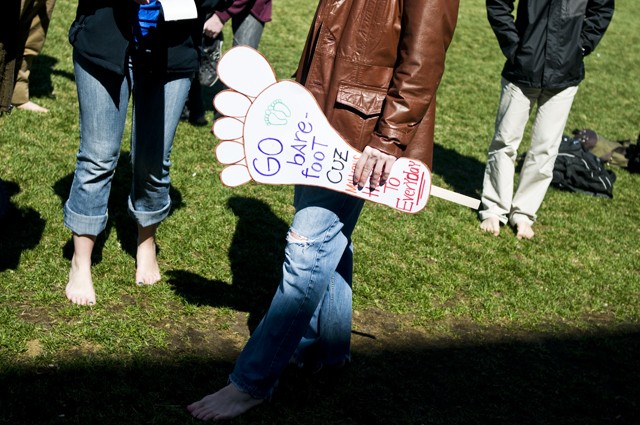 University senior Geoff Enright holds a sign urging students to take off their shoes in front of Coffman Memorial Union on Thursday. 