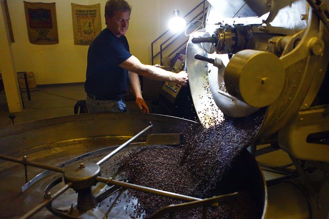 Kevin Larson operates the roaster for Tiny Footprint in Brooklyn Park on Monday afternoon. As the coffee beans come out of the roaster they are mixed in the tray to cool off and prevent burning.