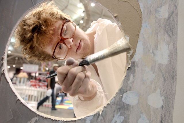 MCAD Junior Brendan Dawson paints a hole Saturday that he cut out of dry wall during the Minneapolis Home Building and Remodeling Expo at the Minneapolis Convention Center.
