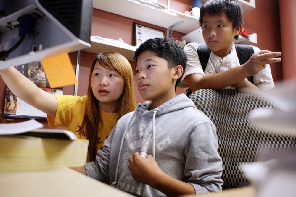 University of Minnesota freshman Kaoxue Vang, left, helps Pao Lee, center, and Pao Xiong, right, with an assignment on dinosaurs. Vang tutors every Sunday night through the Sunday Tutoring Program hosted by the Minnesota Center for Neighborhood Organizing. Vang was tutored in the program when she was in grade school.