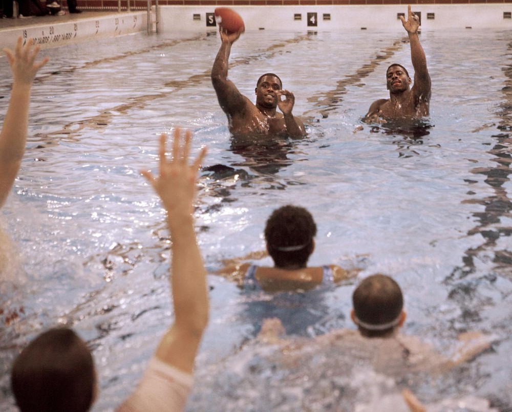 Vikings defensive tackle Fred Evans, left, and linebacker Larry Dean, right, toss footballs to children from the community in a game of 500 Tuesday evening in the Cook Hall pool. The evening started with a healthy dinner and swim lessons for the kids as the physical activity for week six of the Vikings Fitness Playbook weight-management program. 