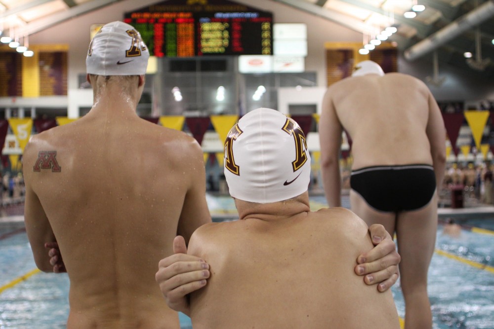 Members of Minnesotas 400-meter medley relay team, Max Cartwright, Ben Griggs, and Zach Bolin wait poolside for their teammate Josh Hall.  Minnesota took 2nd in the 400 medley relay with a time of 3:25.02.