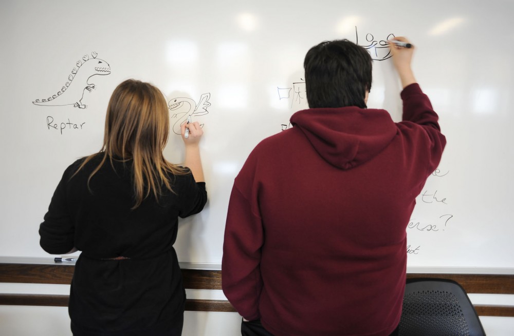 Apolinar, right, and a classmate draw on a whiteboard before their Chicano studies class Tuesday in Folwell Hall. Apolinar was deported when he was in eighth grade when his parents, who are not citizens, were forced to return to Mexico.