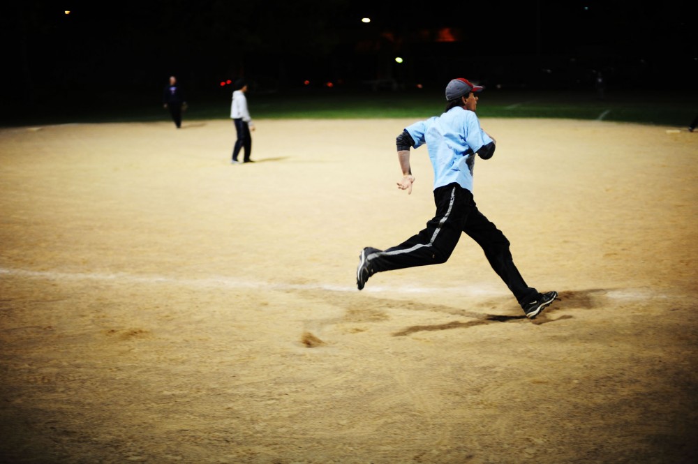 A runner makes a quick dash towards home during a game of softball at the West Bank Softball Fields.
