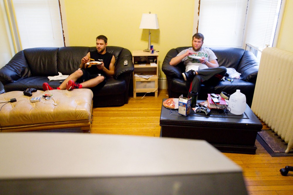 Nick Fehst and Cody Lake, eat pizza and watch sports in the living room of the University House. Both Fehst and Lake have been living in this sober house for about three months.