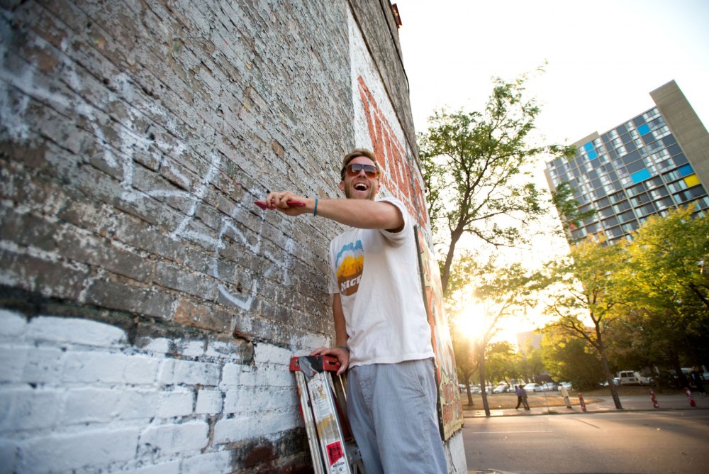 Block party organizer Jake Heinitz laughs while he chips brush off the wall of a parking lot that borders Nomad World Pub, where the block party will be held.