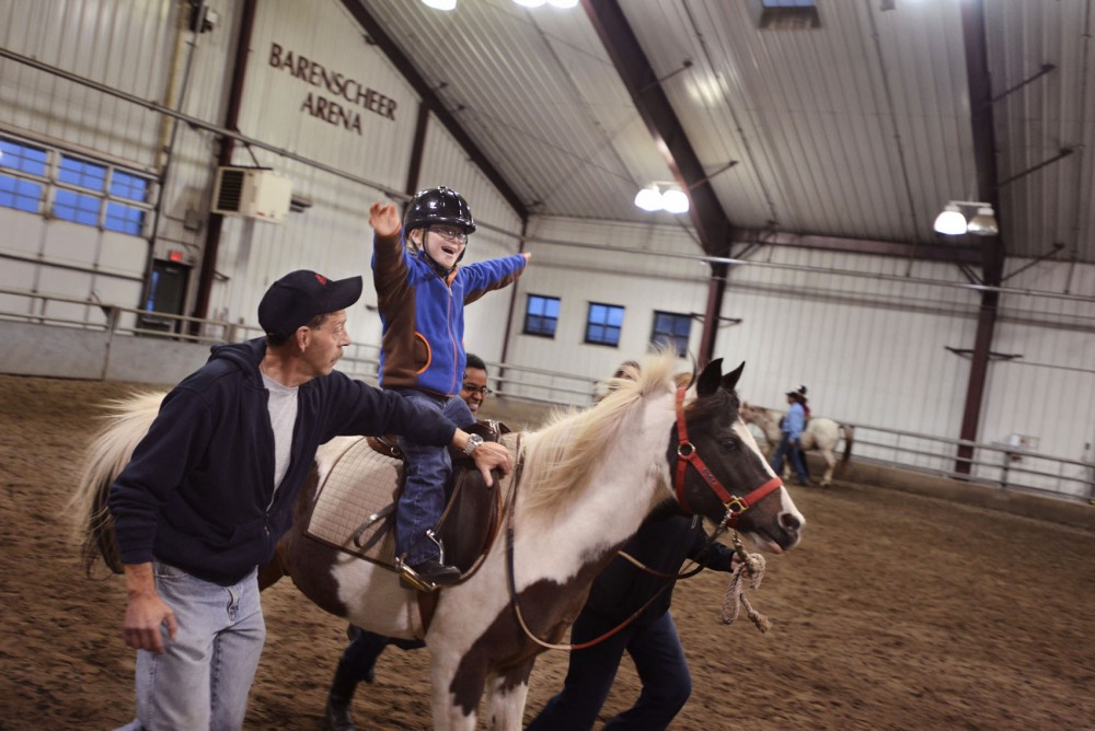 We Can Ride participant Sam Galles gets excited riding Mel, a therapy horse, with volunteers by his side at Barenscheer Arena in St. Paul.