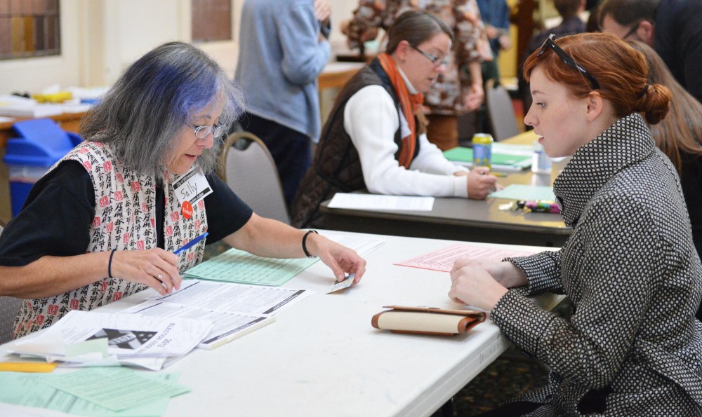 Election judge Sally Downing, left, helps political science senior Jennifer Maes, right, with her registration at the United Church of Christ polling center on Tuesday. Many students chose to register on Election Day.