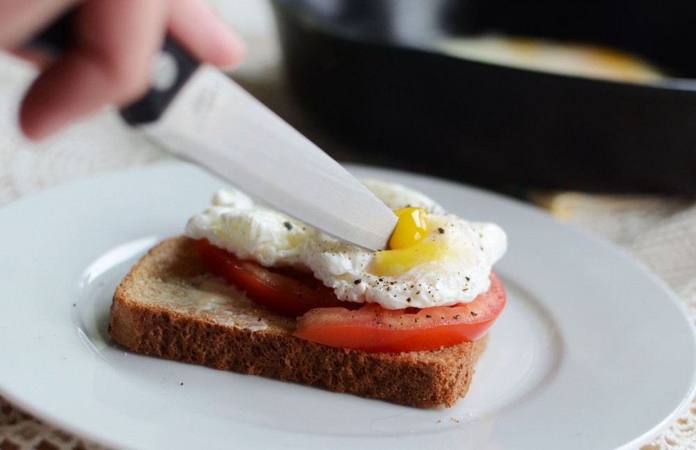 A poached egg served with tomato on top of buttered toast.