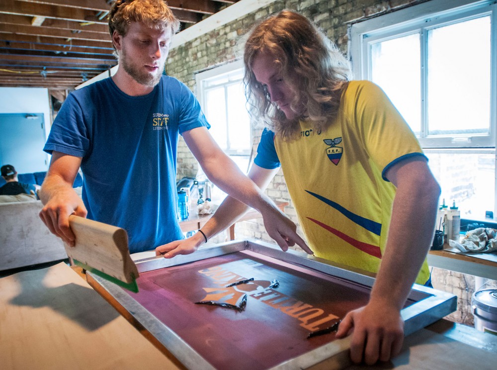 Bioproduct marketing and management junior Drew Swanson, left, and global studies senior Phil Kelly prepare to silk screen their logo onto a board at TurtleKing Workshop Friday, April 26, 2013, in Minneapolis. The TurtleKing co-founders have partnered with the Cedar-Riverside Youth Council and the Minneapolis STEP-UP program to teach local youth how to design, build and sell longboards.
