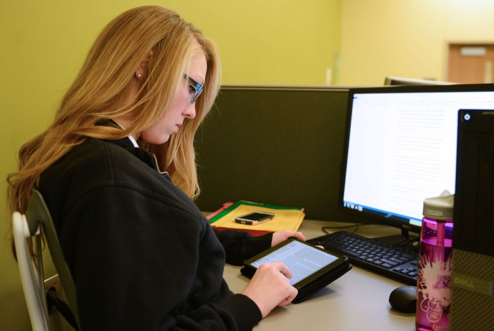Freshman CEHD student Andrea Harpestad uses her University-provided iPad to read and highlight a text while typing a related assignment on a computer.  