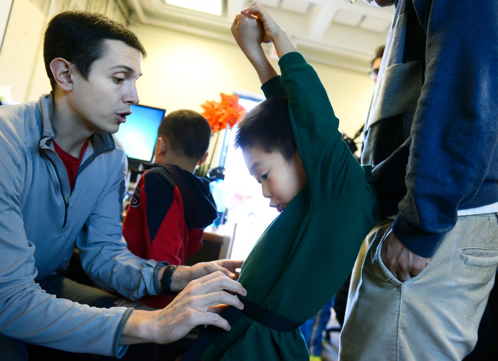 Graduate Assistant Zachary Pope adjusts helps fit 5-year-old Chris Chen with an accelerometer at Williamson Hall on Sunday. The test is for a study to help better understand how young children are affected through home-based excise gaming.