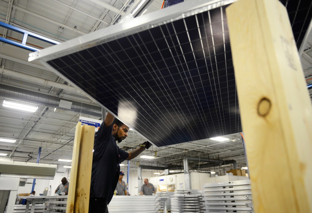 Employee of tenKsolar, Dwayne Blakely, moves solar panels onto a module light table for testing. Innovative Power Systems is working to put solar panels on the green line corridor in hopes of making solar energy more readily available. 