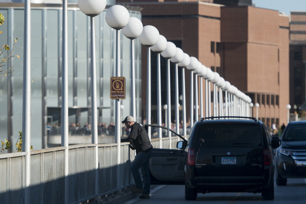 The officer stands next to a sign that reads There is hope make the call on the west side of Washington Avenue Bridge as pedestrians gather on the east side of the bridge on Tuesday, Nov. 8, 2016.
