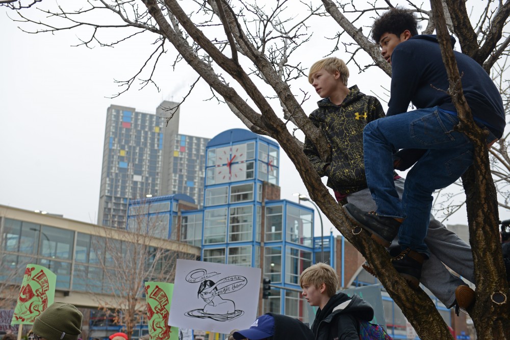 Eighth-graders Lukas Nederloe and Darius Spearman listen to speakers from a tree outside the Humphrey School of Public Affairs on Friday, Jan. 20, 2017. A large group of students from Marcy Open School met protesters at the University to join the march.
