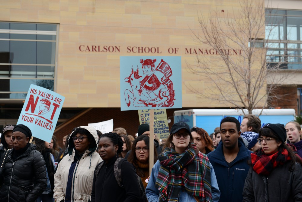 Protesters listen as speakers decry President Donald Trump outside the Humphrey School of Public Affairs on Friday, Jan. 20, 2017. Members of the University of Minnesota art faculty helped create some of the signs used by protesters.