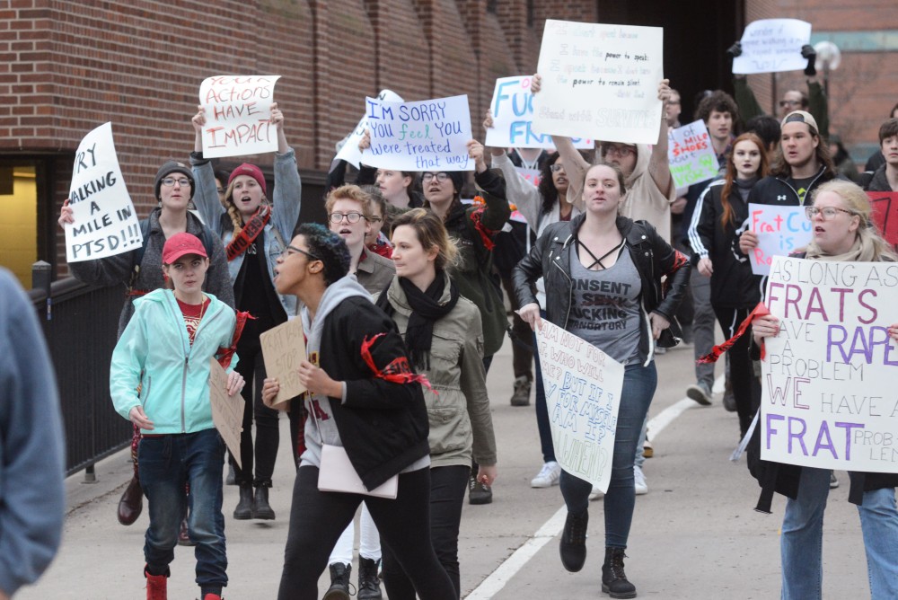 Protesters chant as they cross behind Greek life members on Tuesday on East Bank. Members of Greek life held their 4th annual Walk a Mile in Her Shoes event to make a stance against sexual assault.