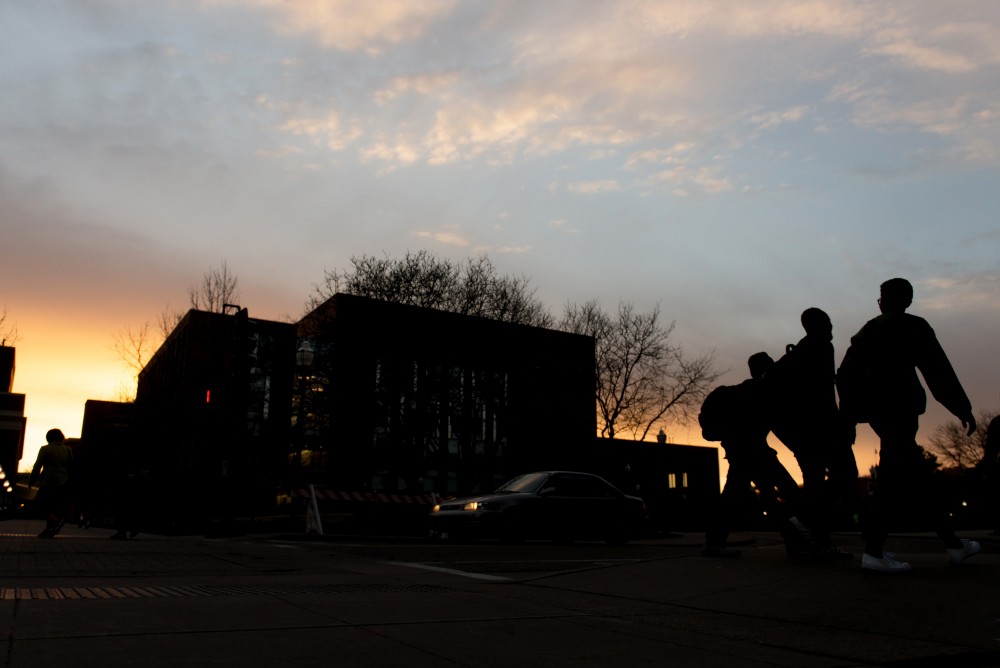 The sun sets as a group of three students walk past the Recreation and Wellness Center.  