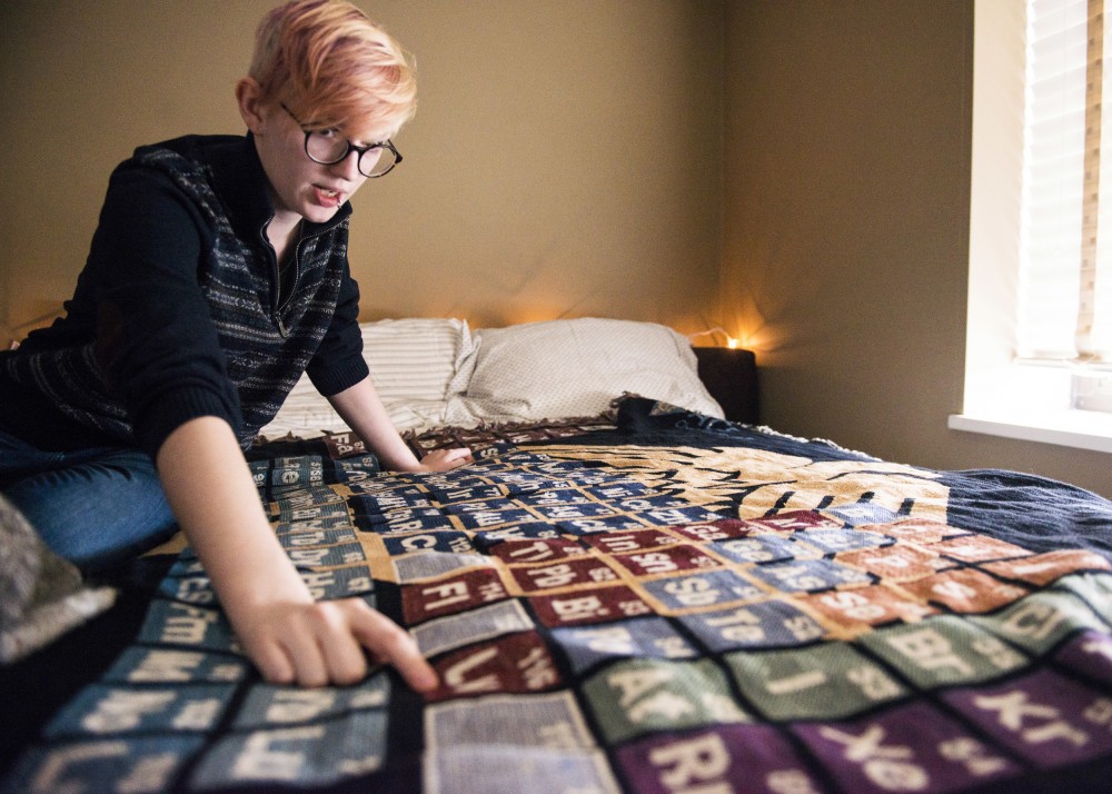 Vee Livermore, who suffers from chronic migraines, drapes their bed with a chemistry-themed blanket. They point to the element Livermorium, named after a distant relative from England.