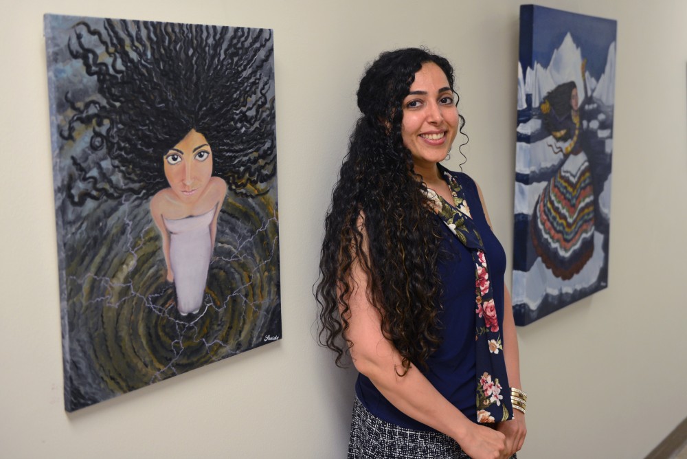 Saeide Mirzaei stands beside her oil paintings exploring the experiences of immigrant women in the U.S. on the garden level of Appleby Hall on Sept. 20, 2017. 