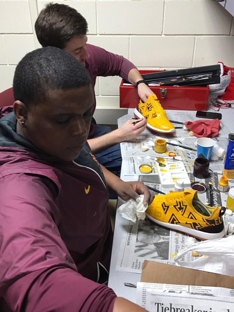 Recruiting Assistant and Graphic Design Specialist Will Henry works with Graphic Designer Niko Alexander to paint new designs onto shoes for the Gopher football team on Thursday, Sept. 28.