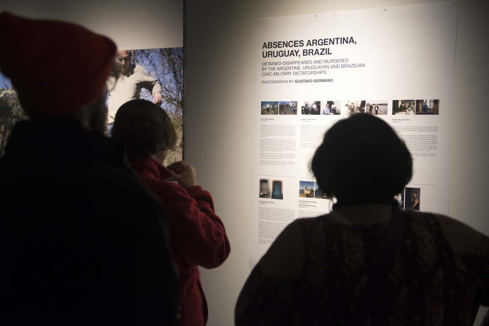 Viewers of Gustavo Germanos learn about the photographs at the exhibit opening at Regis East on West Bank on Friday, Nov. 10. Germanos exhibition entitled Absences showcases people detained or murdered by civic-military dictatorships in Argentina, Uruguay and Brazil.