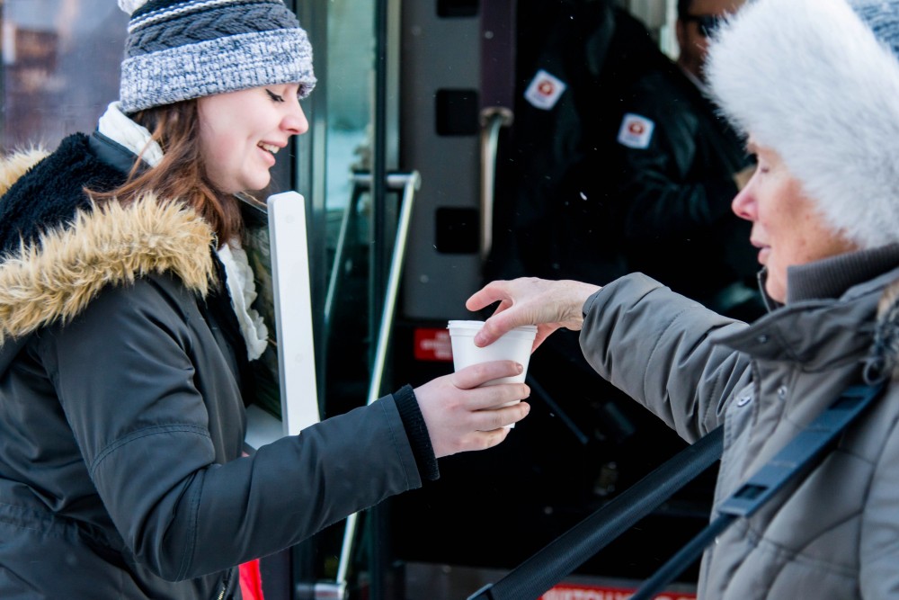 Shirley Arendt, right, offers a hot beverage and snacks to students in Como on Wednesday, Jan. 31. Every Wednesday morning, Arendt and other volunteers from Southeast Christian Church prepare and distribute coffee, hot chocolate and cookies to commuters and Como residents along 15th Avenue.
