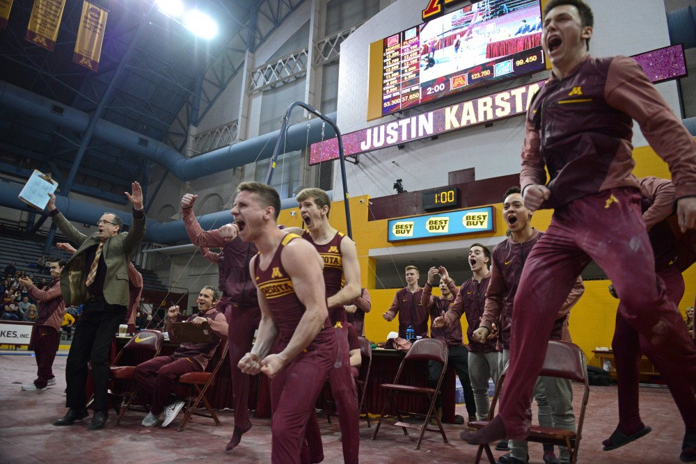 Teammates cheer for Justin Karstadt after sticking his landing on the pommel horse during a meet at Maturi Pavilion on Sunday, March 18.