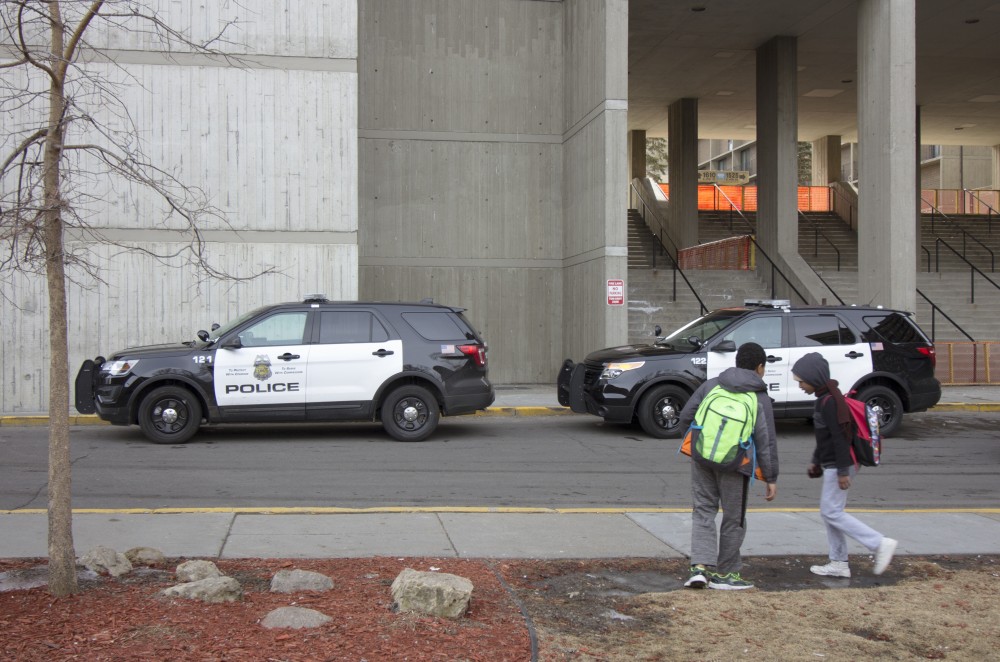Two children walk past police cars parked outside Riverside Plaza on Monday, March 19. Residents of the Cedar-Riverside neighborhood want to see more East African officers policing their community.