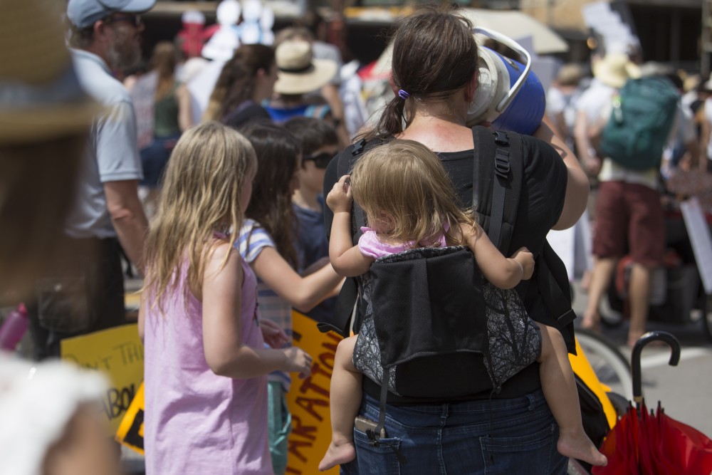 A marcher takes a drink from a jug as a child hangs in her backpack carrier at the Free Our Future march on Saturday, June 30 in downtown Minneapolis.