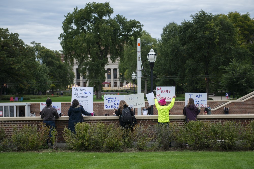 Members of Students for a Democratic Society wave signs above the Coffman Memorial Union bus stop before an event protesting Supreme Court Nominee Brett Kavanaugh on Thursday, Oct. 4. 