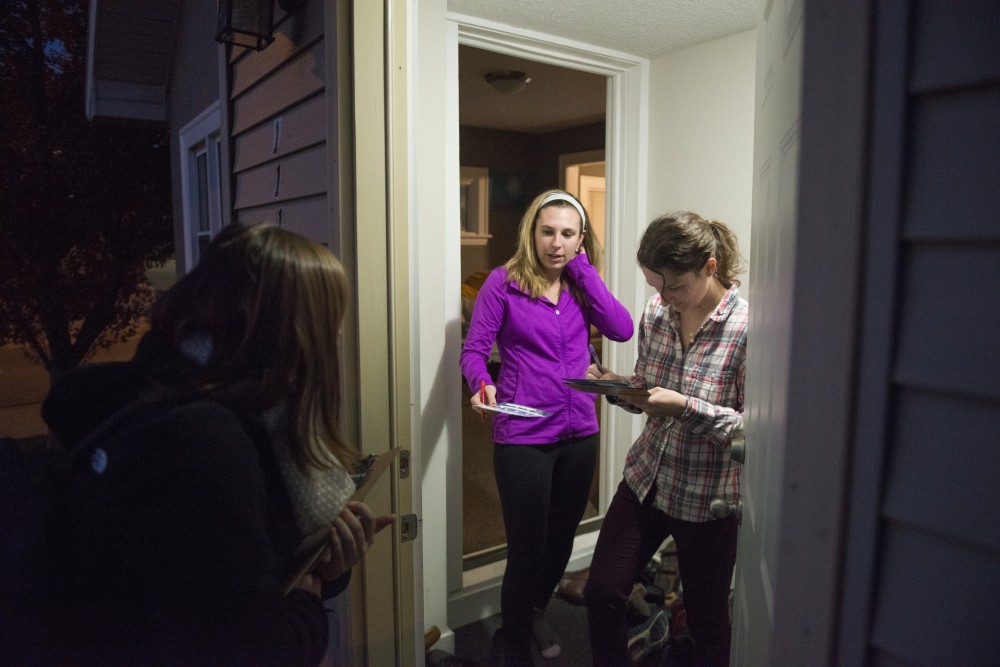 Michelle Jancaric, left, and Carlie Derouin agree to fill out voter pledges for Michaela Muza, a campus organizer with the DFL Youth Coordinated Campaign, in their doorway  on Tuesday, Oct. 23 in the Como neighborhood.