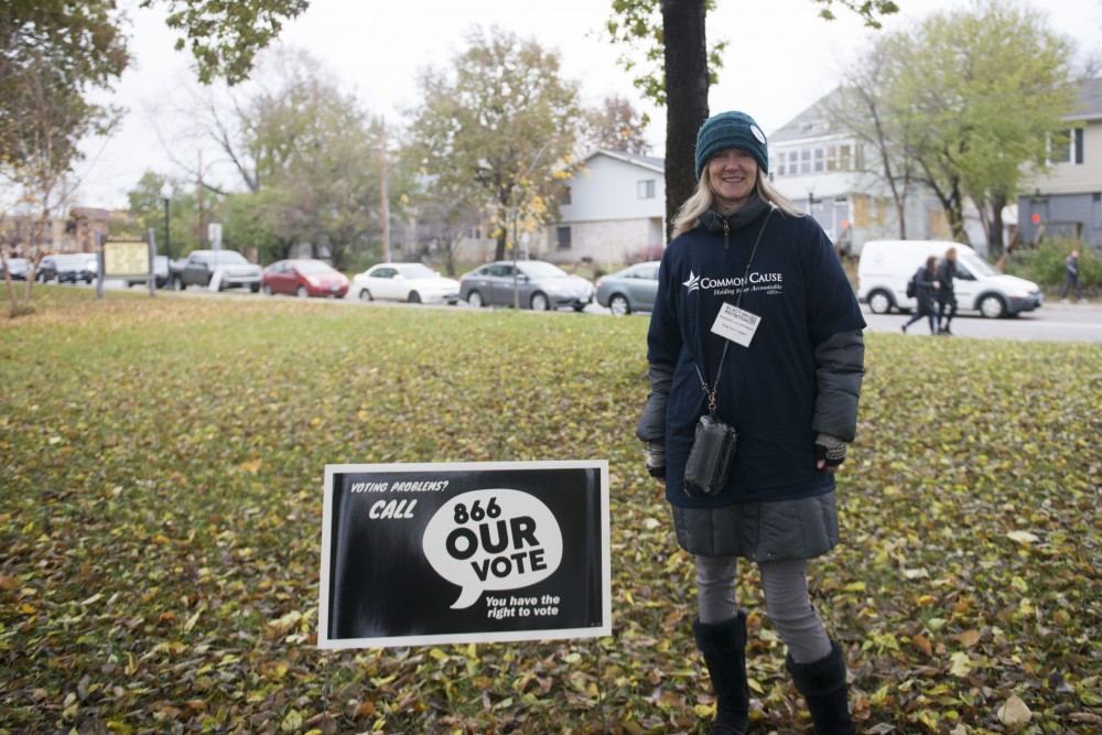 Volunteer for Common Cause Cary Anderson stands next to a sign she put up at Van Cleve Park on Tuesday, Nov. 6. Common Cause provides polling protection and aims to combat voter suppression. 