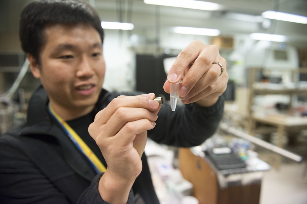 Ph.D candidate Joseph Um holds a magnet up to a vial of nano wires in a clear solution on Tuesday, Feb. 12 in Keller Hall on the East Bank campus.