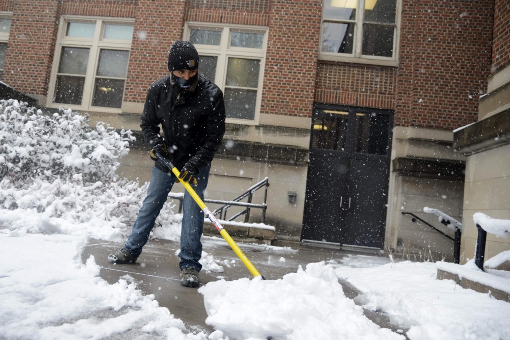 Asgedom Yohannes shovels snow off the sidewalk behind Lind Hall on Wednesday, April 10. 