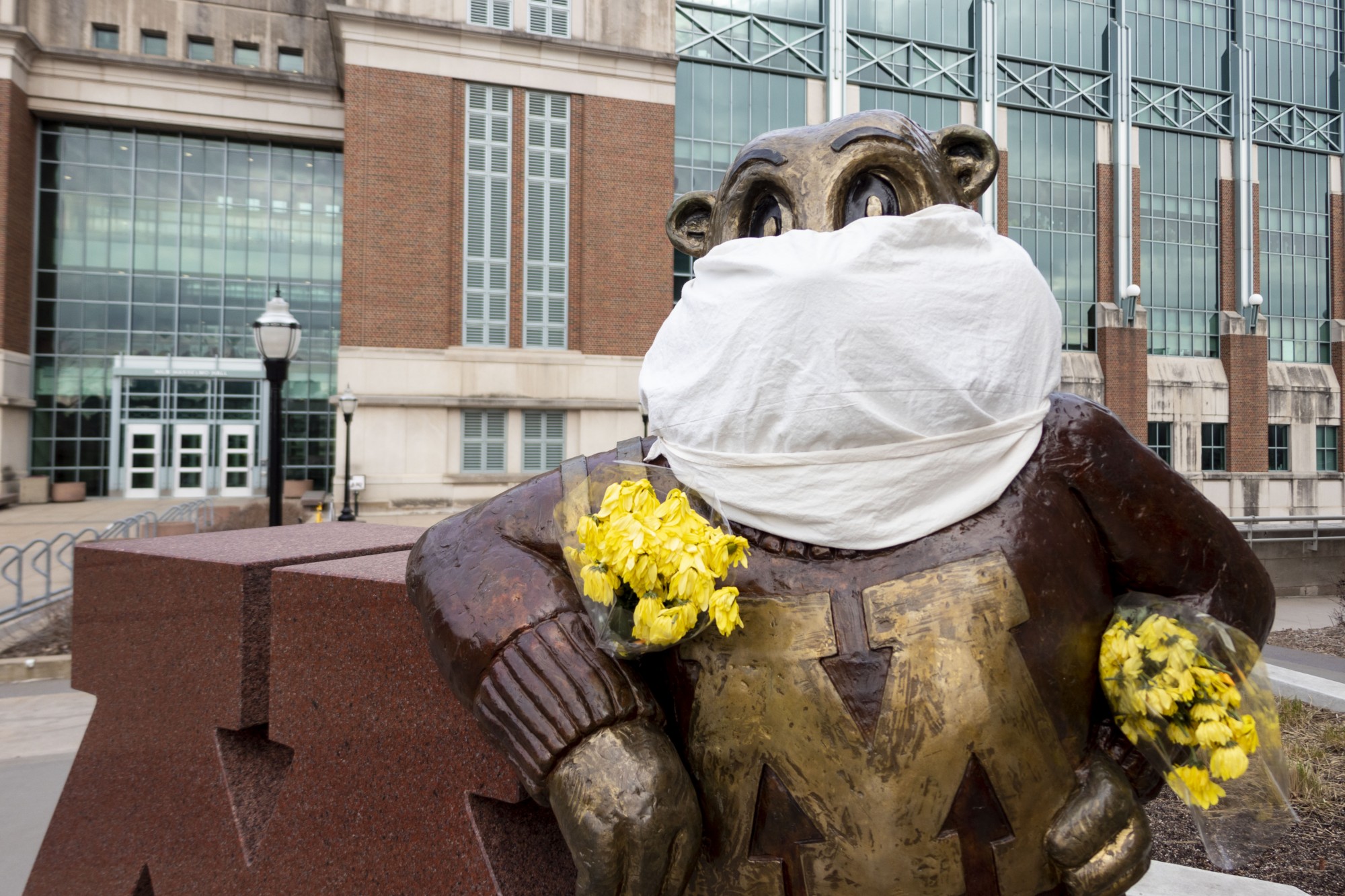 A cloth mask and bouquet of flowers are seen on the Goldy statue outside Coffman Memorial Union on April 1, 2020. 