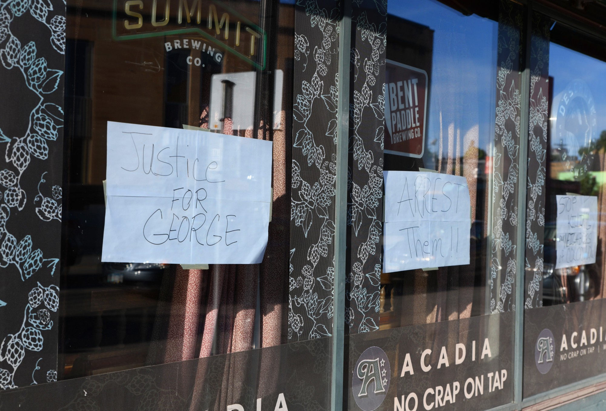 Signs reading “Justice for George”, “Arrest Them!!” and “Stop Killing our Neighbors of Color” hang in the windows of Acadia Café in the Cedar-Riverside neighborhood on Thursday, May 28. 