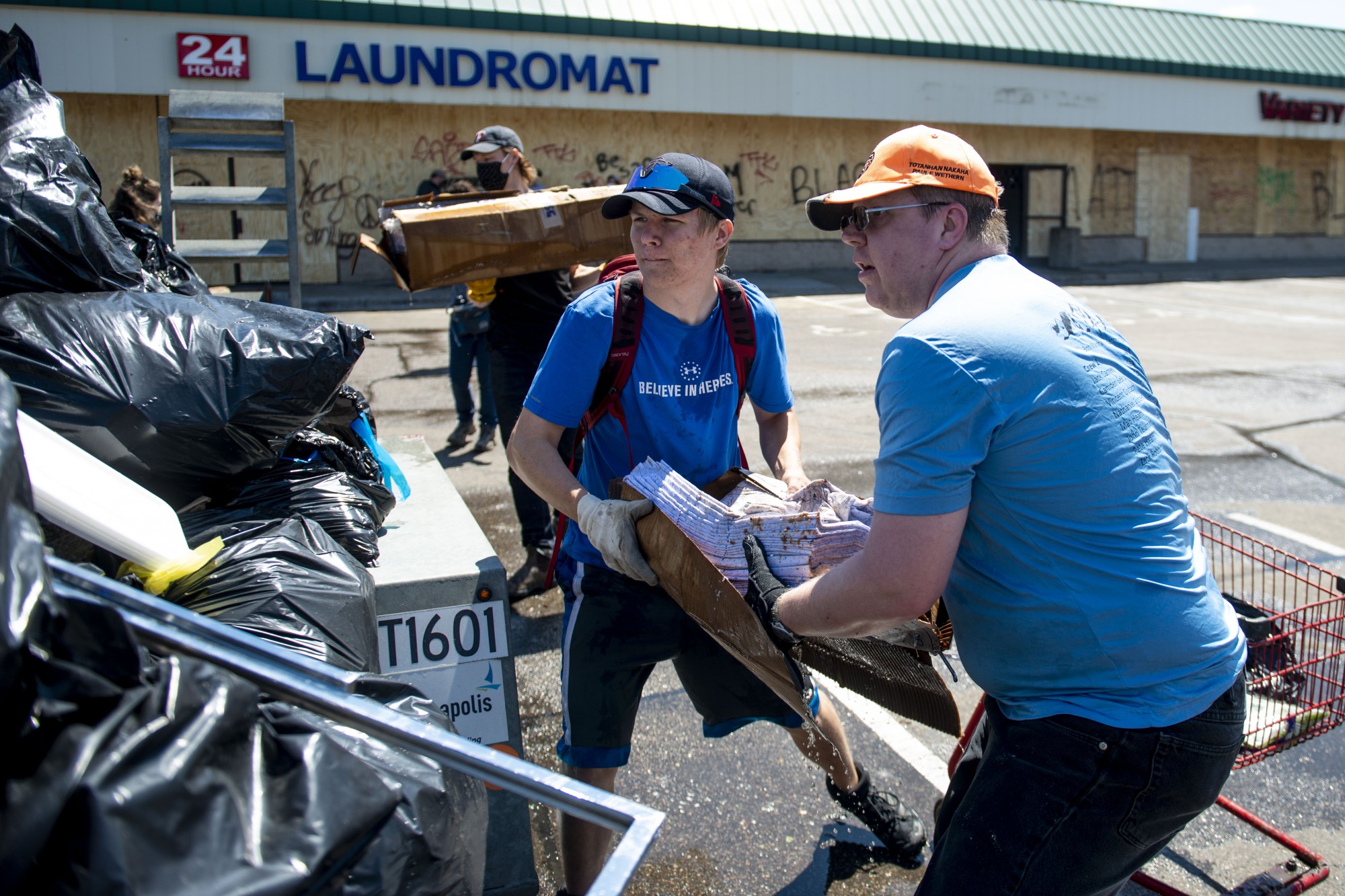 Kyle O., left, and Andy Murphy, right, of Boy Scout Troop 196, work to lift debris into a dumpster outside of Dollar Tree near the Minneapolis 5th Police Precinct following another night of riots on Saturday, May 30. 