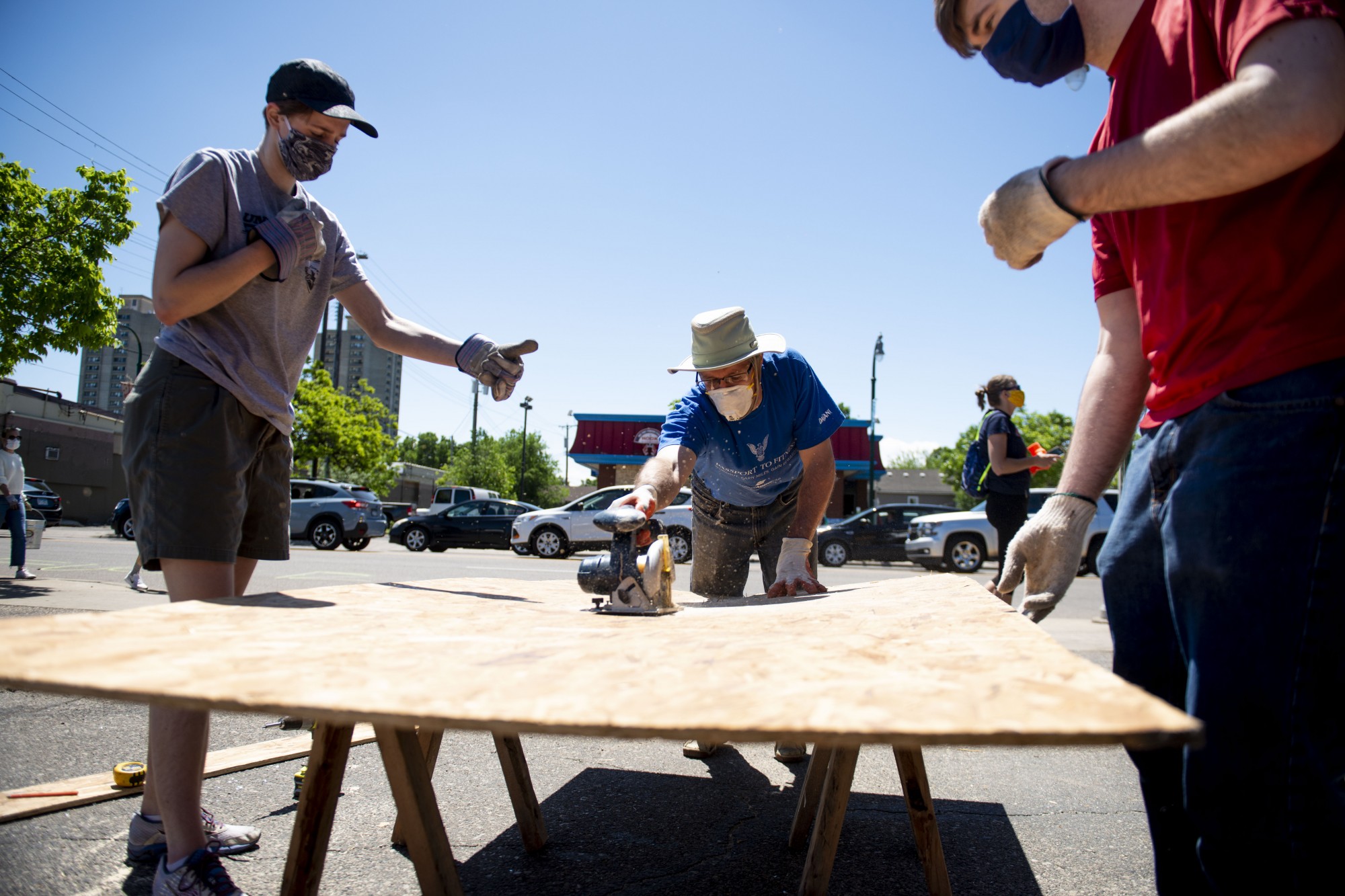 Alaina Bohrer, left, guides Kevin Bohrer, center, as he cuts a piece of plywood to be used to protect local businesses near the Minneapolis 5th Police Precinct following another night of riots on Saturday, May 30. 