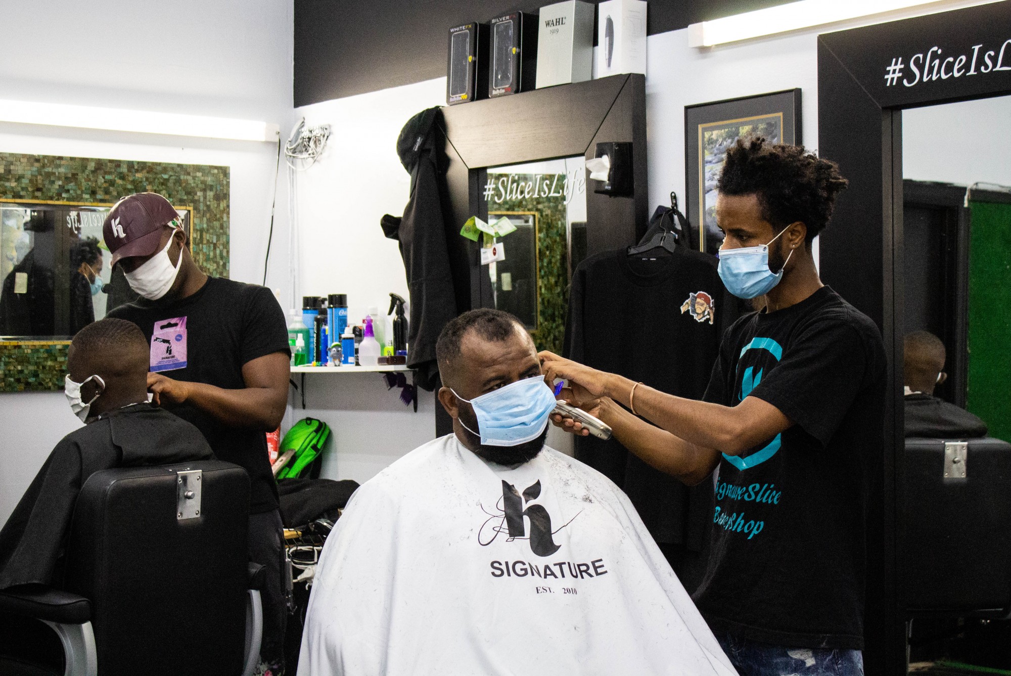 Mohammed Aliyu (left) and Henok Gemeda (right) style customers hair at K Signature Slice Barber Shop on Lake Street in Minneapolis on Monday, July 13.