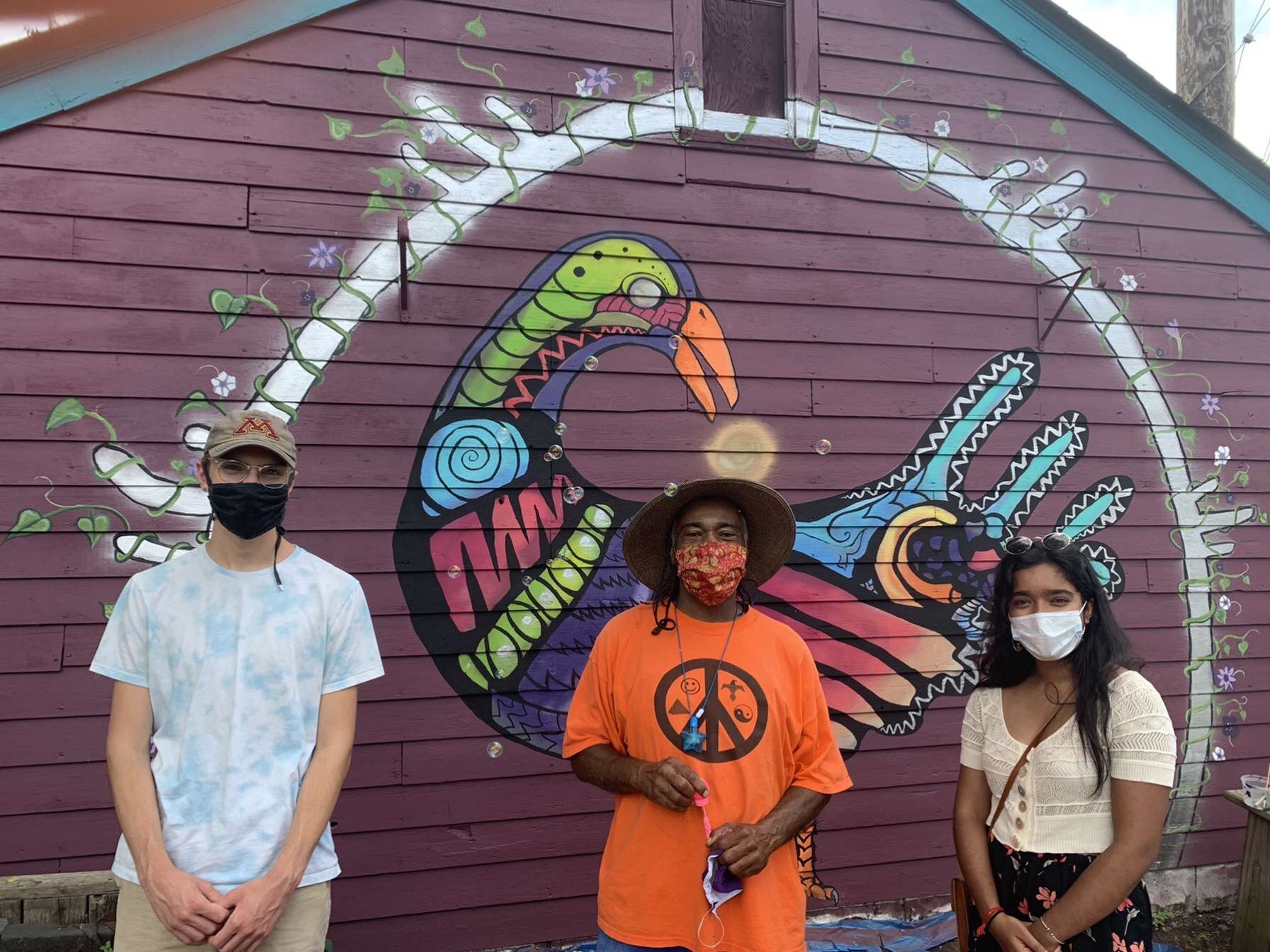 Robert Glisky, Melvin Giles and Sneha Sinha stand in front of a mural in the Peace Garden in the St. Anthony neighborhood of St. Paul. (Photo courtesy of Engineers Without Borders)