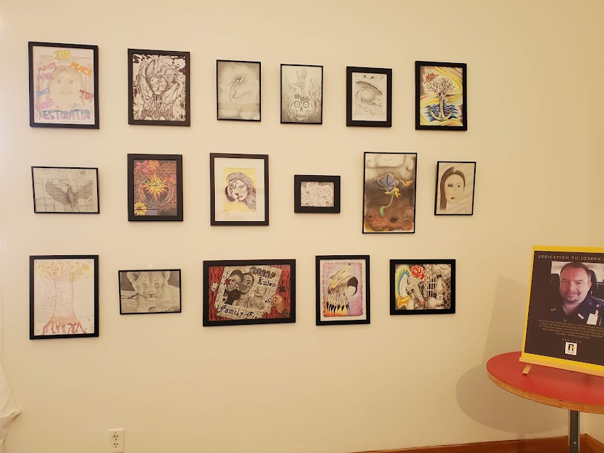 Some of the pieces included in the Transformation: Art From the Inside exhibition hung next to a sign honoring Joseph Gomm. Courtesy of Art From the Inside.