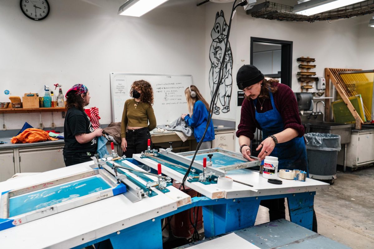 Bohemian Press President Josh (right) tests a screen-print while Minnesota Daily Reporter Sommer Wagen (second from left) interviews club attendees. Printmaking as a medium is good for community-building because of reproduction-centered processes.