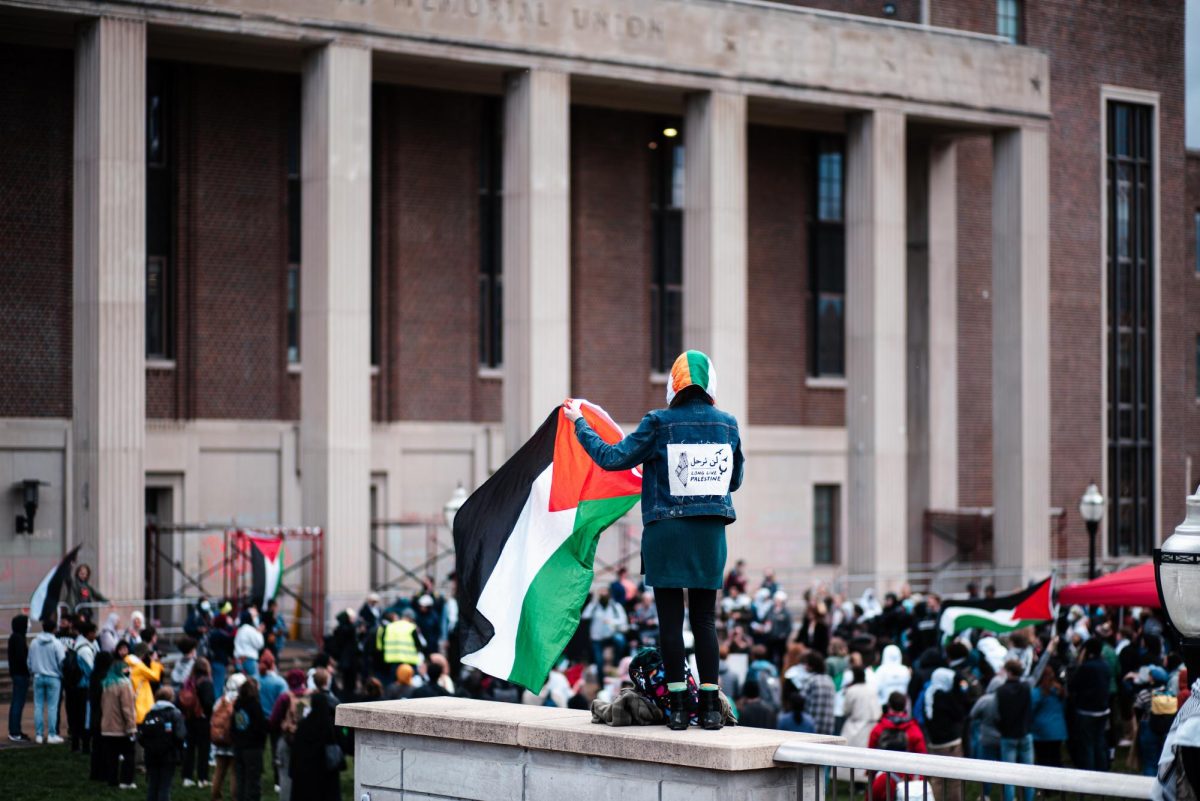 A student waves a Palestinian flag against a backdrop of protestors gathered outside of Coffman Memorial Union on Tuesday.