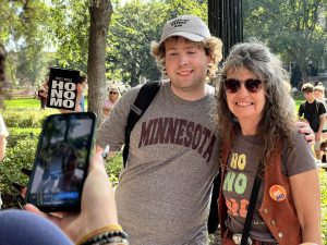 A student in a "Legalize eating ass" hat poses for a picture with Sister Cindy.