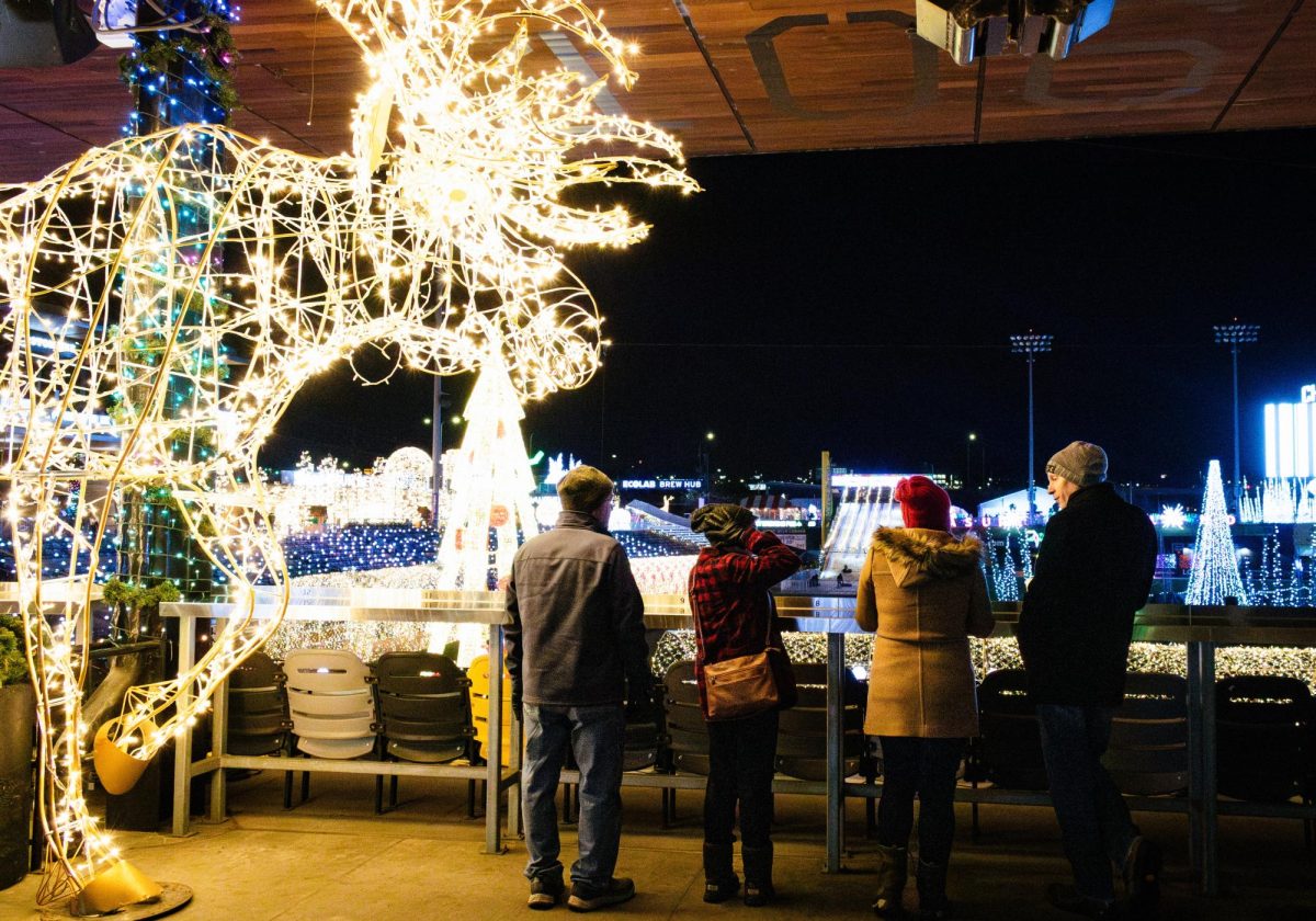 (left to right) Scott and Arlene Duchan, their daughter Amy, and son-in-law Greg Sippl stand next to an illuminated moose while overlooking Glow Holiday Festival’s Christmas trees, tube slide, and tunnels, and other lighting displays on CHS Field.